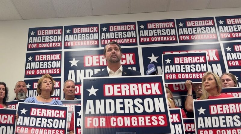 Derrick Anderson, the GOP candidate, stands behind a platform with signs.